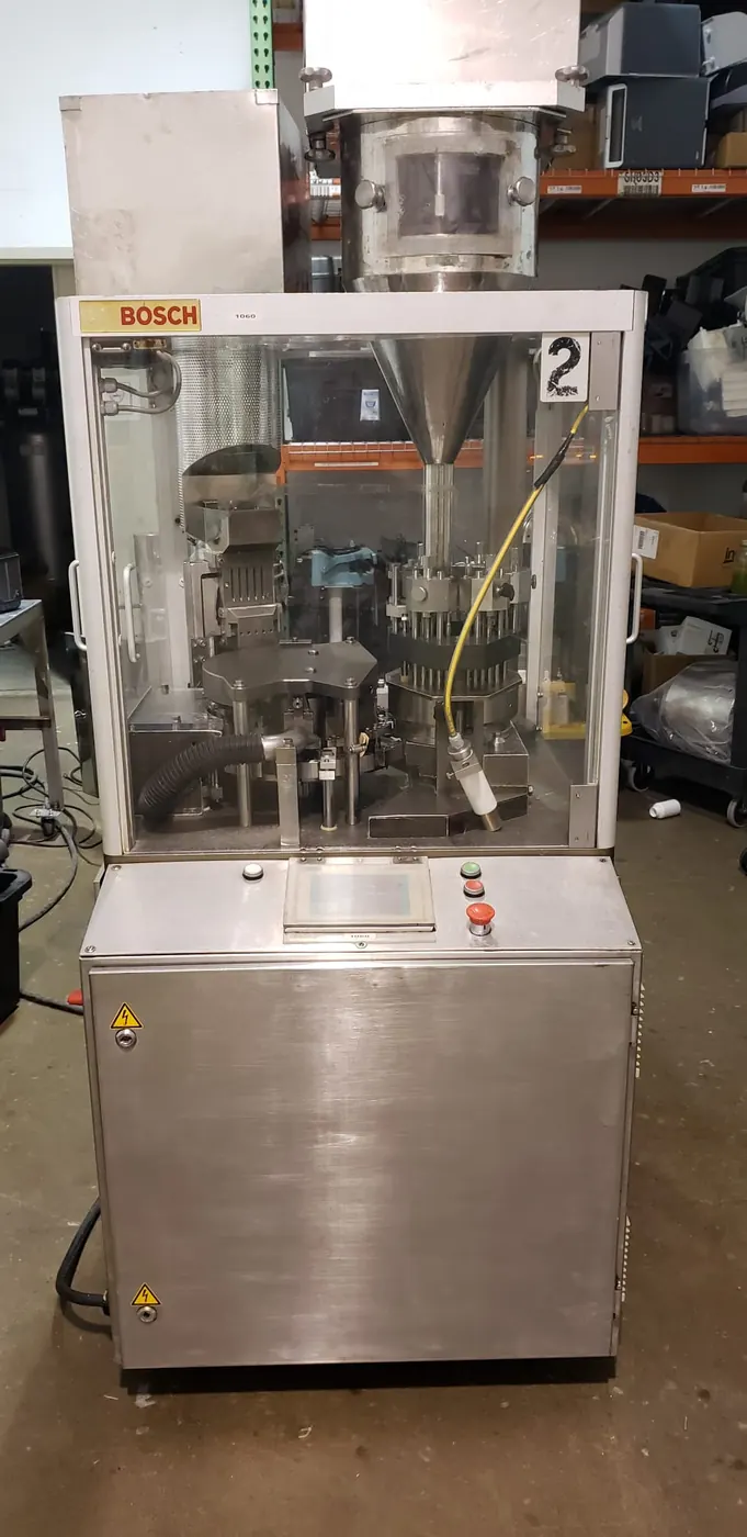 Bosch automatic capsule filling machine with guard doors closed and a stainless dosing hopper mounted above the filling turret.