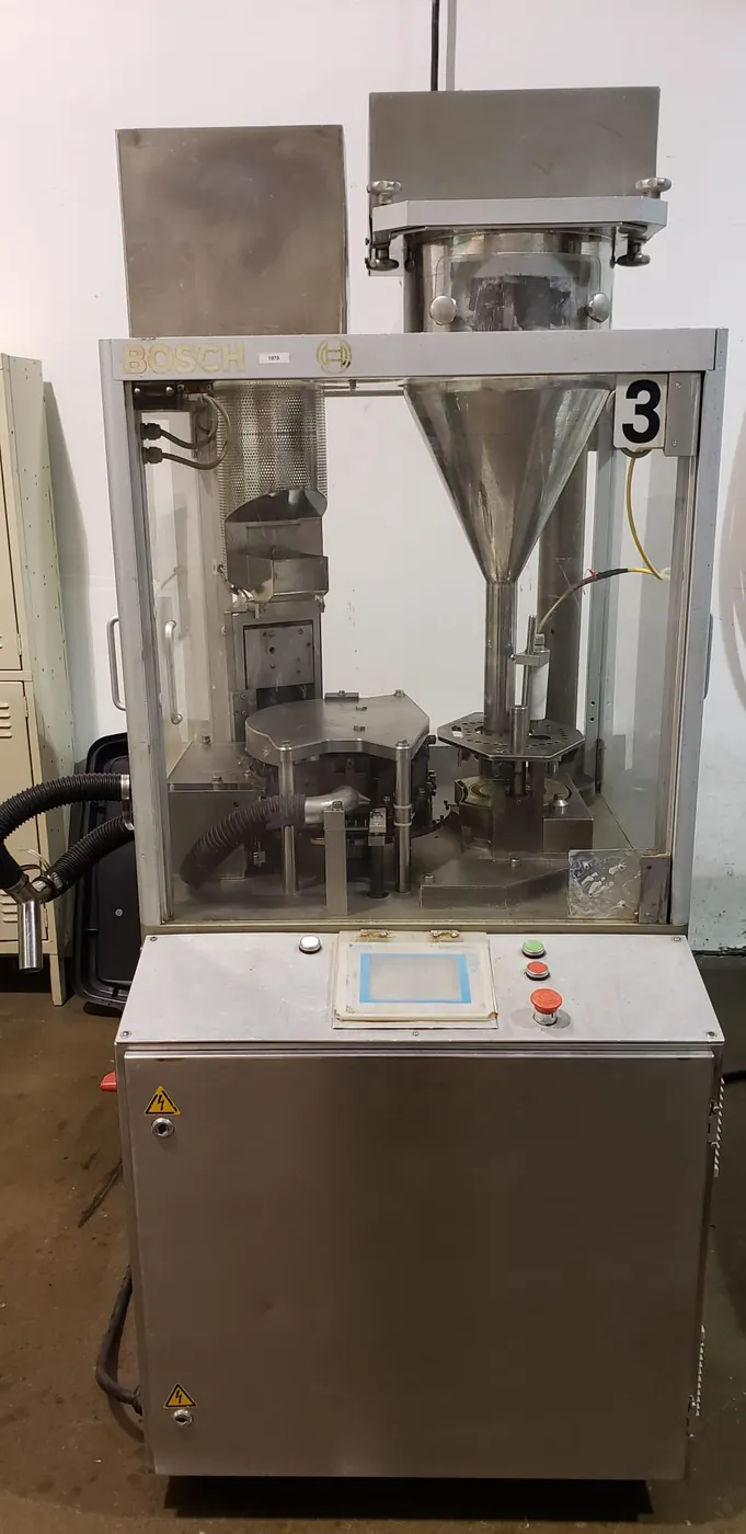 A second Bosch capsule filling machine in a stainless cabinet, control panel at waist height and a polycarbonate-guarded filling turret above.