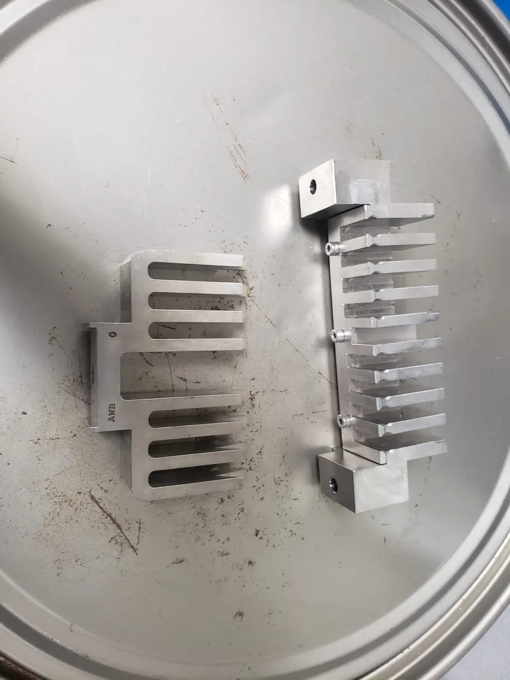 Two machined aluminium change parts with combed fingers resting on a stainless drum lid.