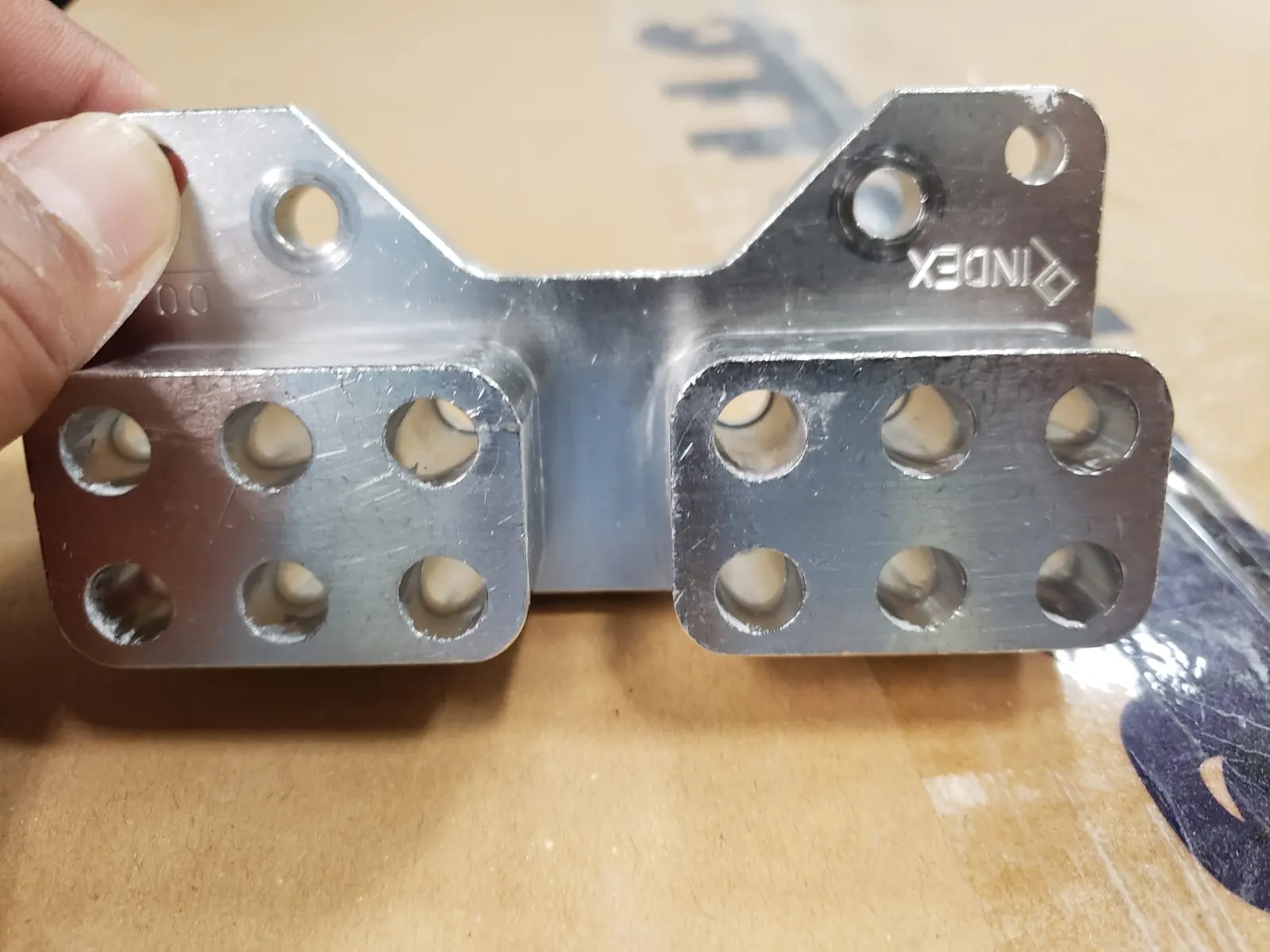 Hand holding a machined aluminium segment with twelve bored pockets, stamped INDEX and size 00 on the mounting flange.